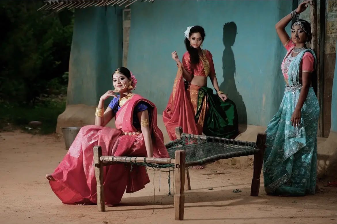 Three women in colourful sarees staged on a wooden cot