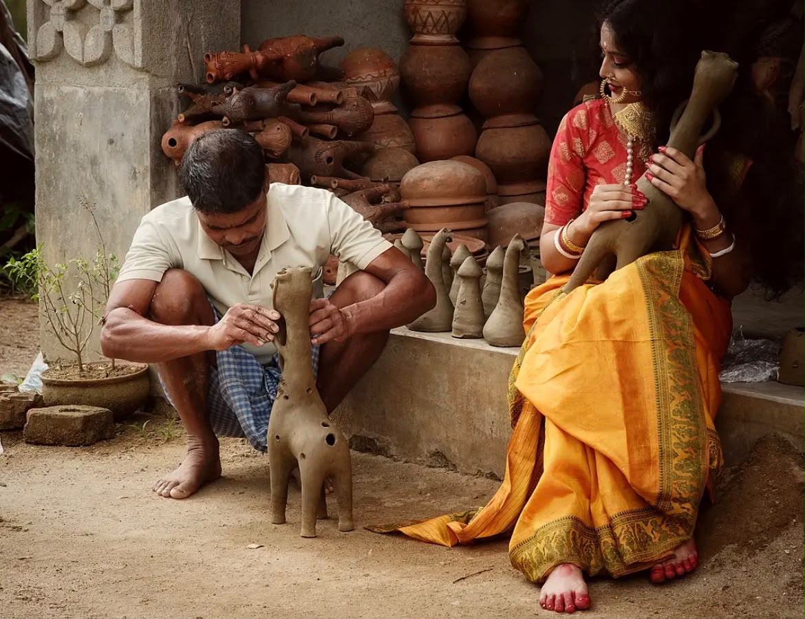 A potter shaping clay beside a model admiring the terracotta work